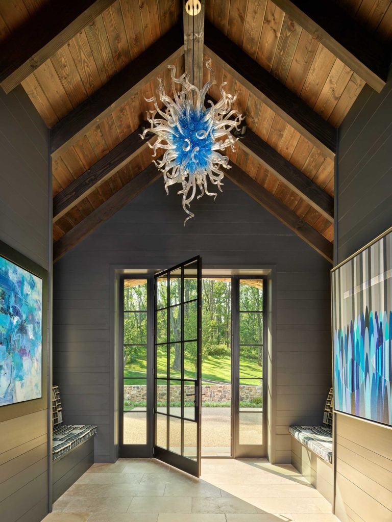 Contemporary entry foyer with vaulted ceiling, exposed beams and wood decking, modern glass chandelier, built in benches and dark metal framed door