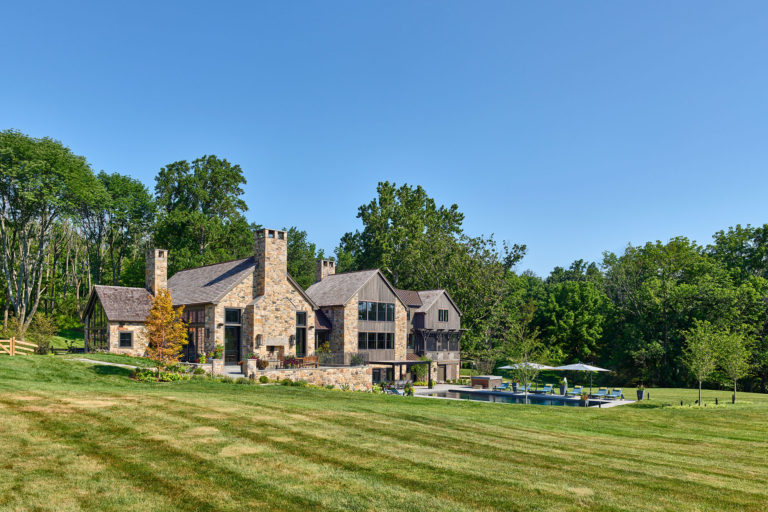 Rear view of contemporary farm house with stone and board and batten siding exterior, a metal roof, pool, and patio with fireplace