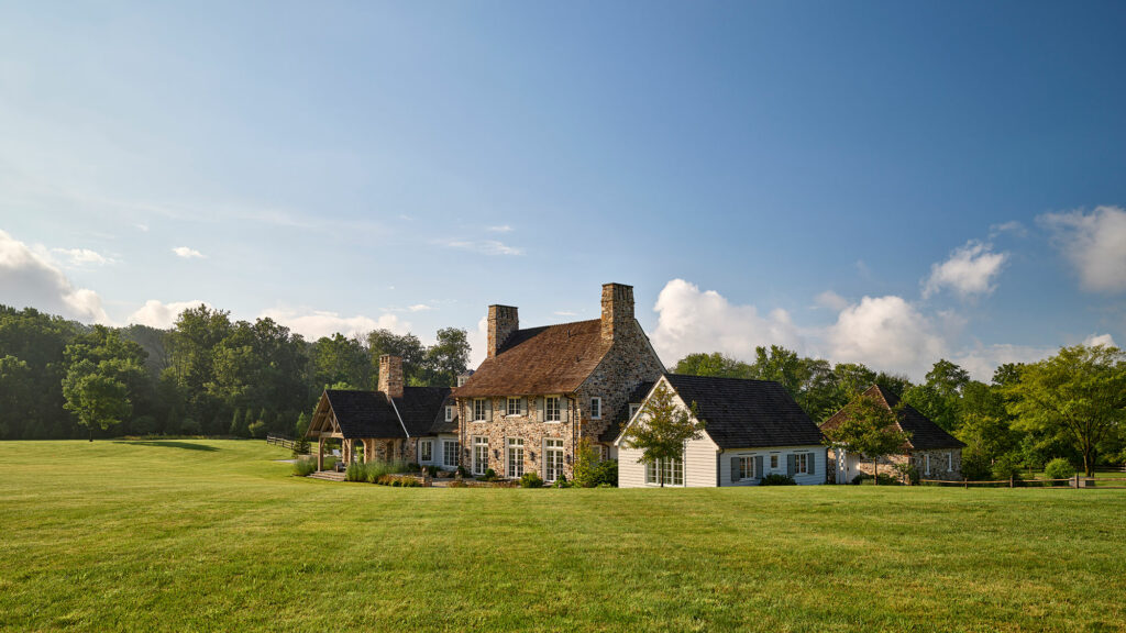 Rear exterior of Chestnut Fields, a farmhouse with stone and siding walls and cedar shake roof.