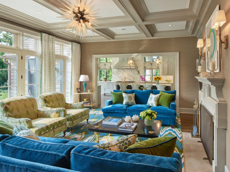 family room with blue couches, a coffured ceiling and fireplace open to new kitchen in the renovation of a 1950s colonial revival home